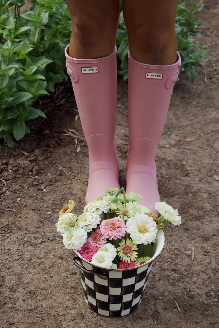 Pink rain boots beside a checkered bucket of zinnias