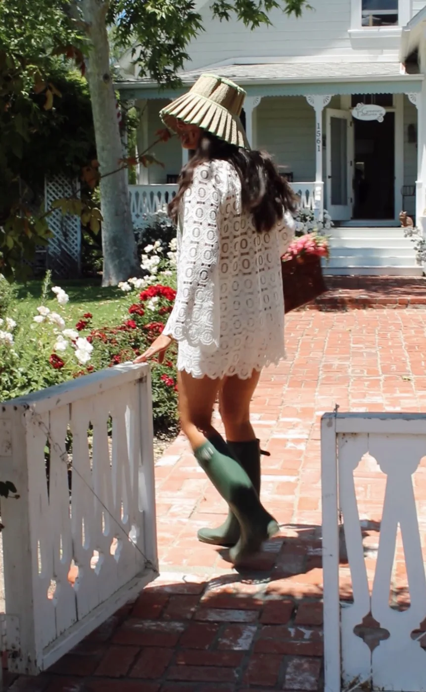 Woman in white lace and green boots walking through a white garden gate
